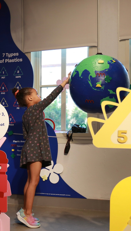 A girl reaching up to touch the interactive globe in the Plastic Universe exhibition